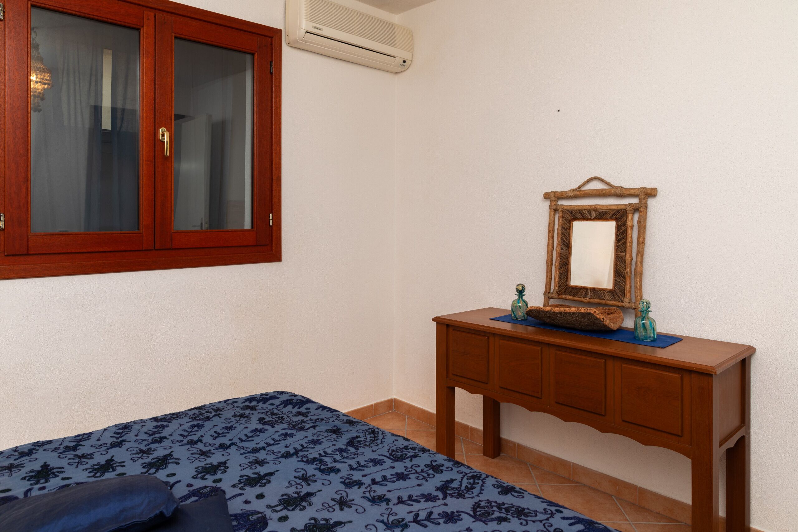 A bedroom with a bed, a wooden dresser, a mirror, and an air conditioning unit.