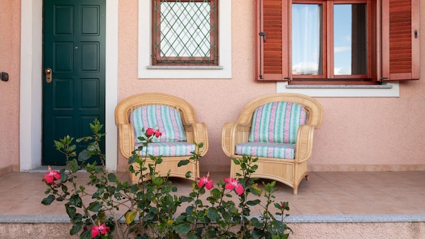 A building facade with a green door, a window with a metal grid, and two wicker chairs with striped cushions. - Casa Marzia by Wonderful Italy (Olbia)