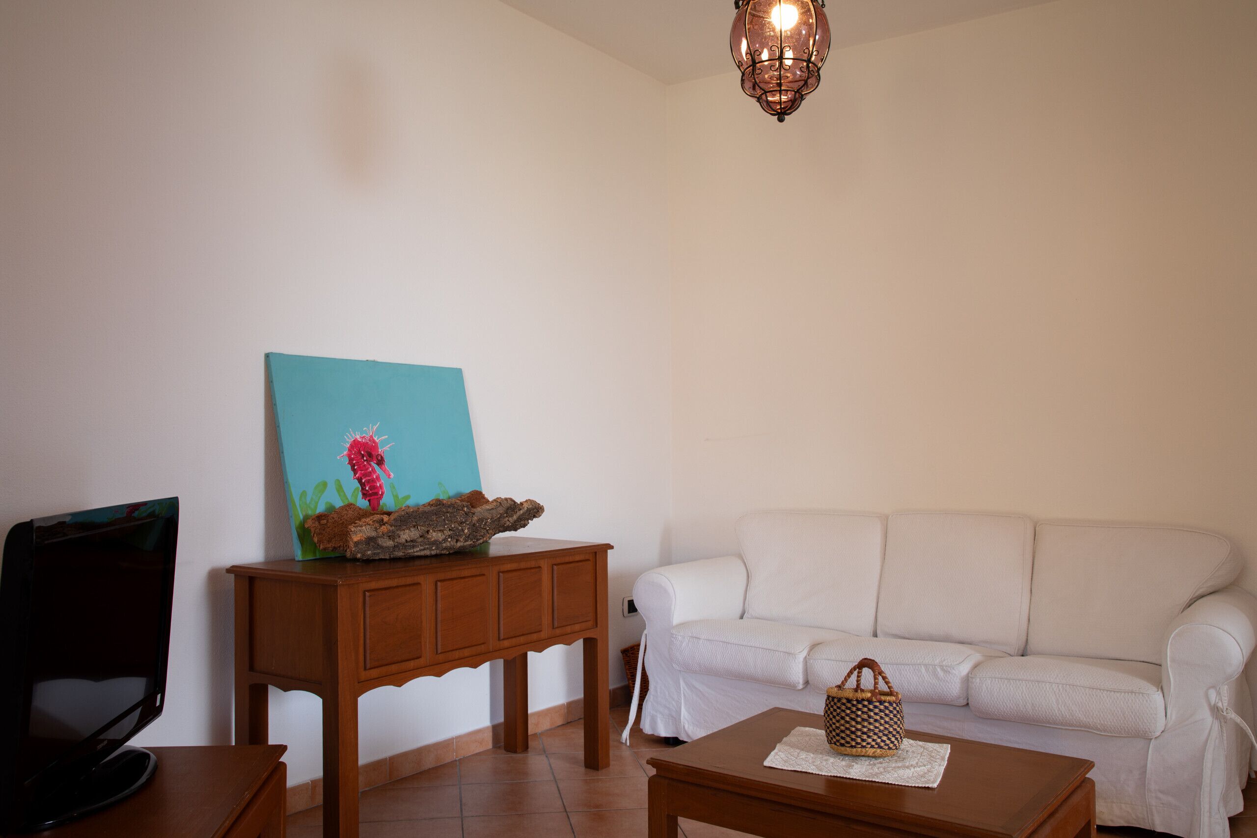 A living room with a white sofa, a wooden coffee table, a TV on a stand, and a painting on a wooden table.