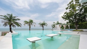 Une piscine à débordement à l’eau d’un bleu cristallin, entourée de palmiers et agrémentée d’un belvédère blanc.