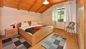 A wooden bedroom with a bed, nightstand, chair, and window with curtains.