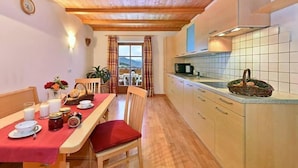 A dining area with a wooden table set for breakfast, a kitchen with tiled backsplash, and a view through a window.