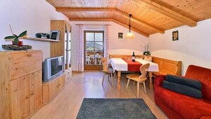 A cozy room with a wooden ceiling, a dining table with chairs, a red sofa, and a television on a wooden cabinet.