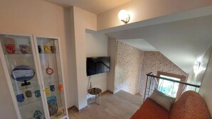 A living room with a sofa, a glass cabinet with decorative items, a flat-screen TV, and a staircase leading to an upper level.