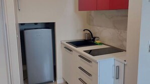 A compact kitchen with a built-in refrigerator, a sink with a faucet, and a red cabinet above the countertop.