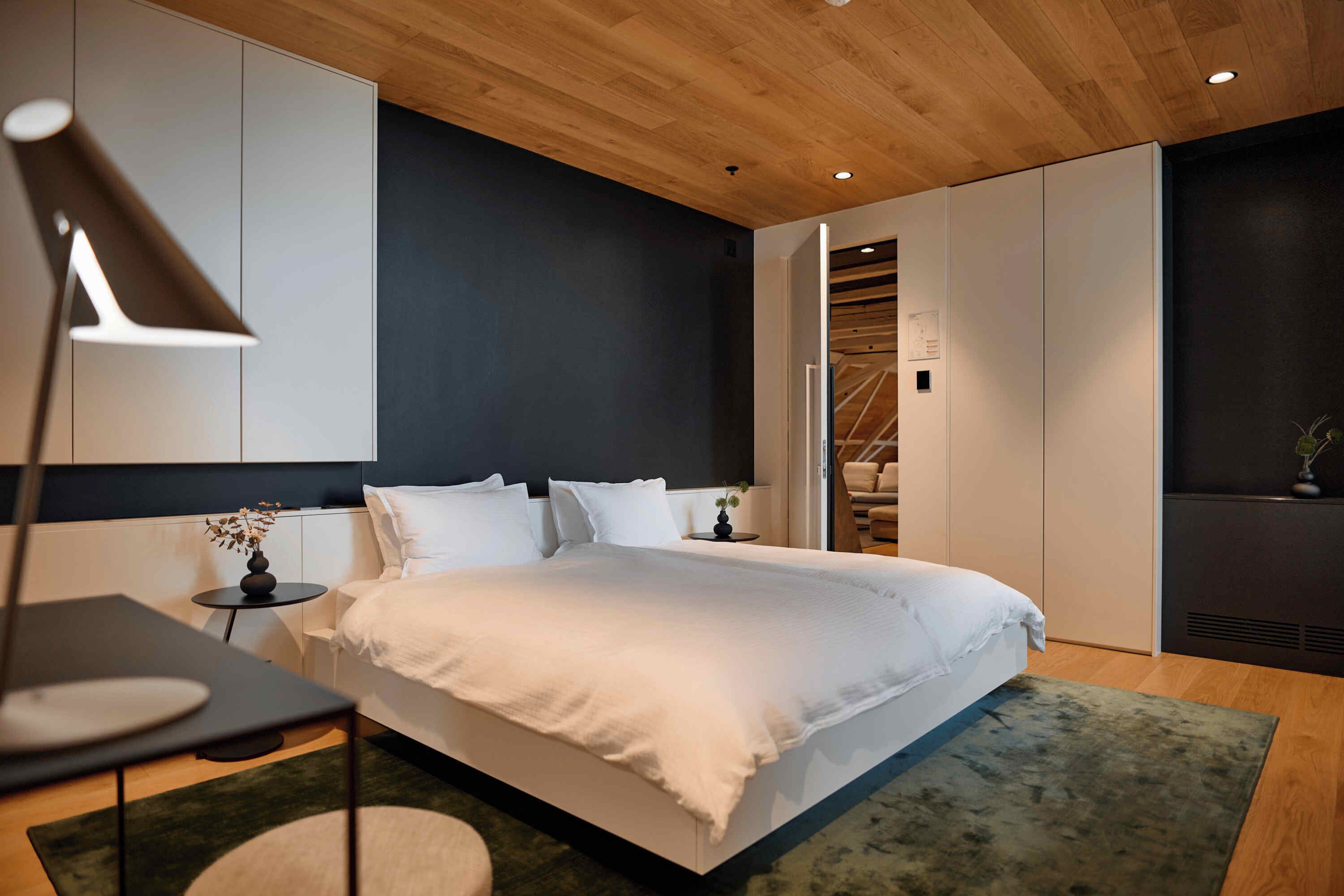 Un dormitorio moderno con una cama grande, una mesita de noche, una lámpara y vistas de una escalera de madera.