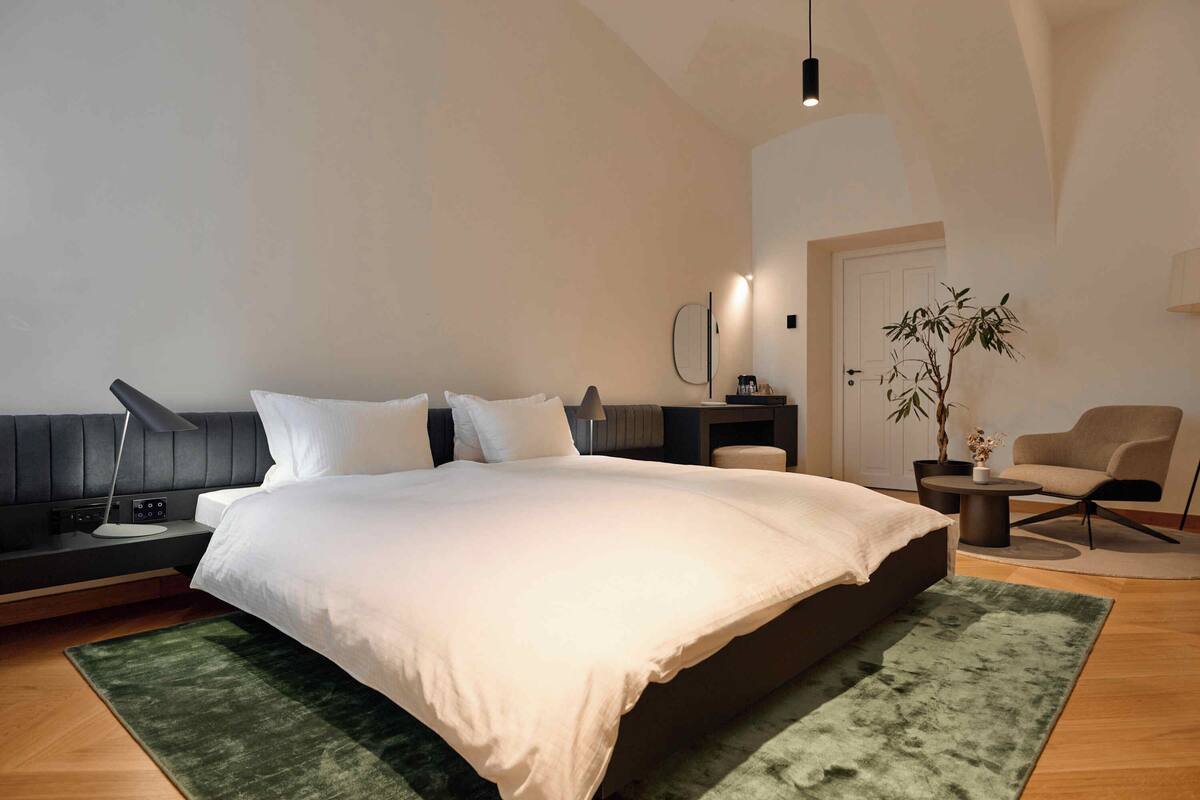 Ein modernes Schlafzimmer mit einem großen Bett, Nachttischen, einem Beistelltisch, einer Lampe, einem Sessel und einem Blumentopf.