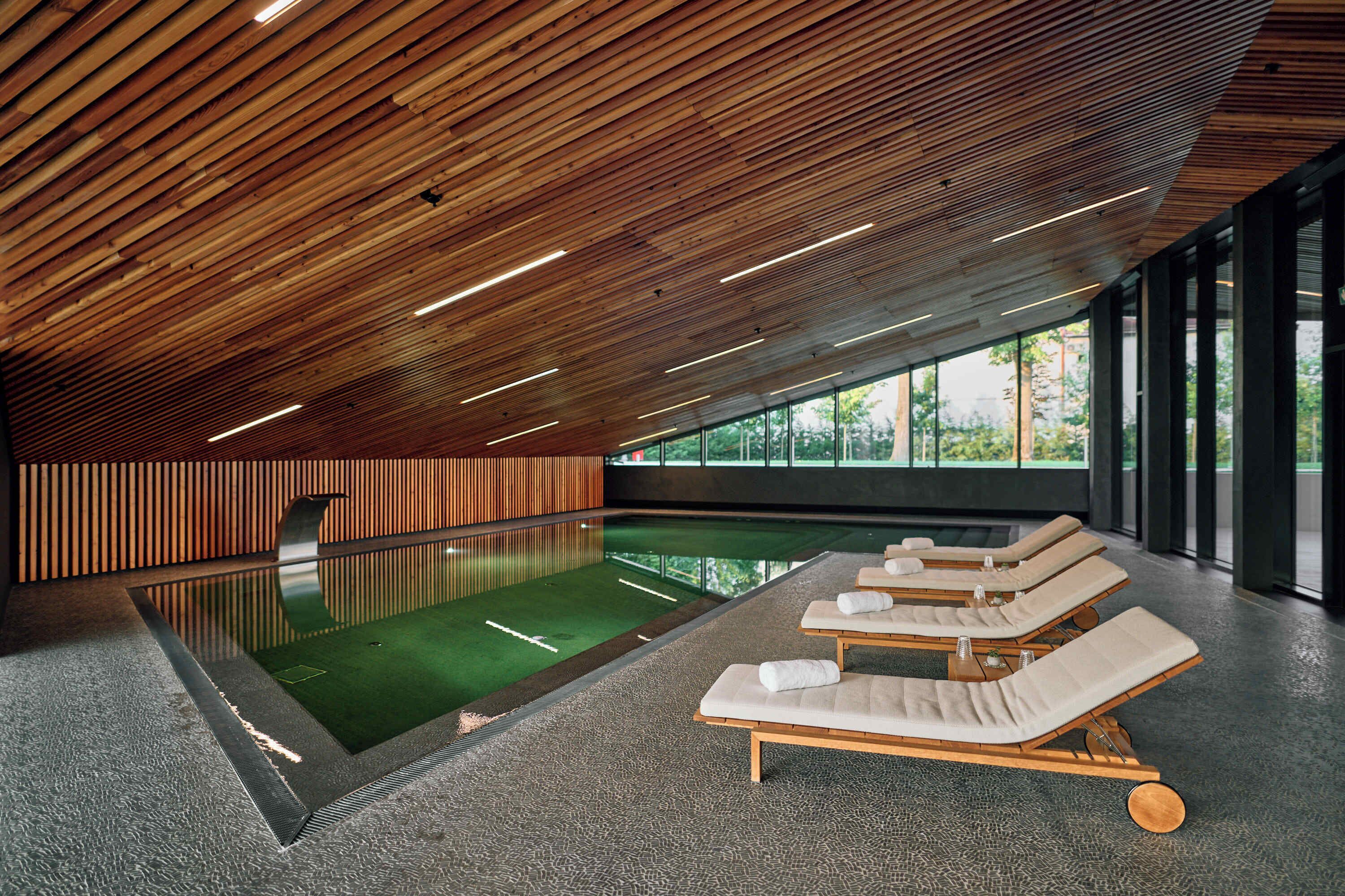 Ein moderner Poolbereich im Innenbereich mit Holzbalkendecke und Liegestühlen.