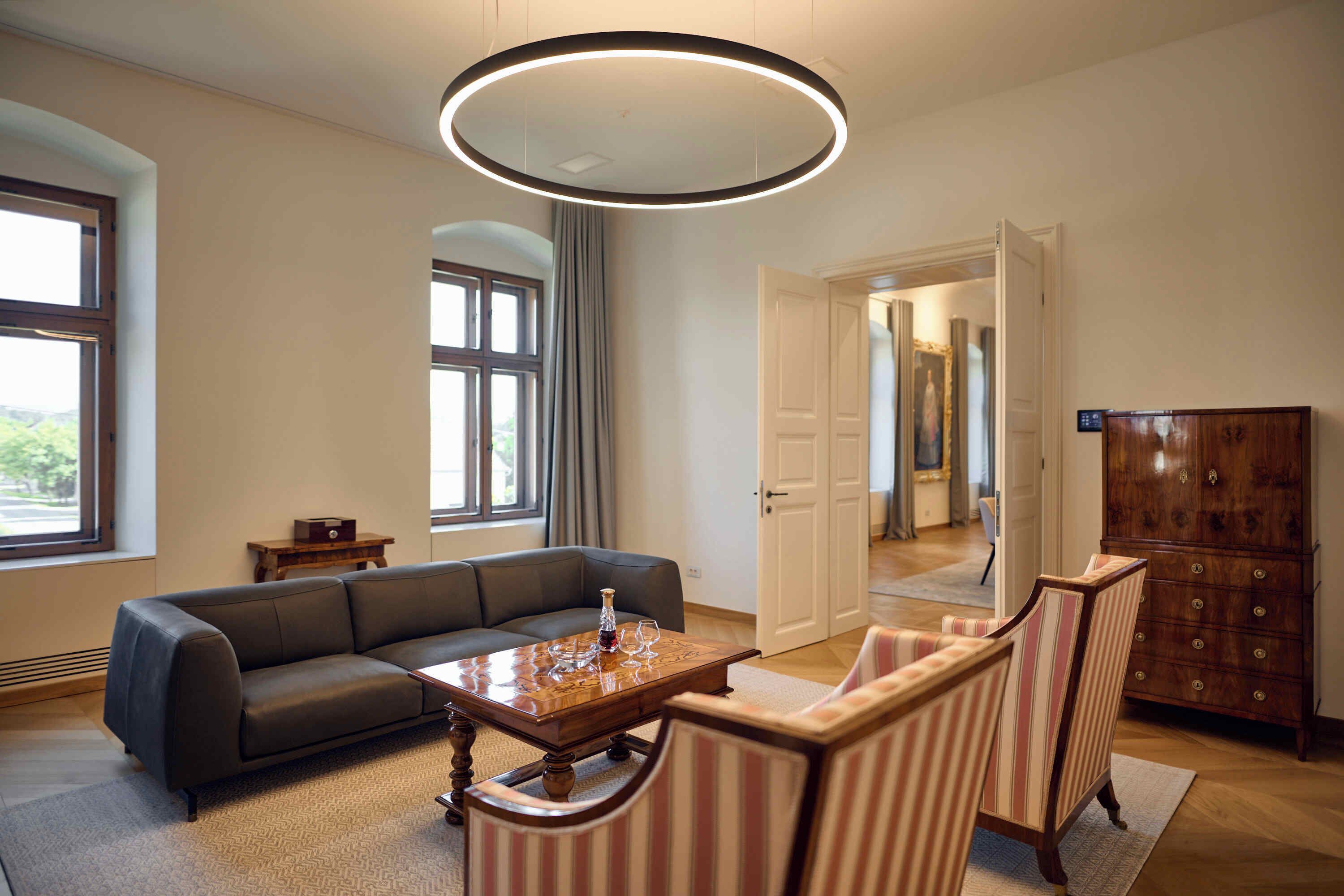 Una sala moderna con un sofá seccional, una mesa de centro de madera, sillones a rayas, un mueble de madera y una lámpara de techo circular grande.
