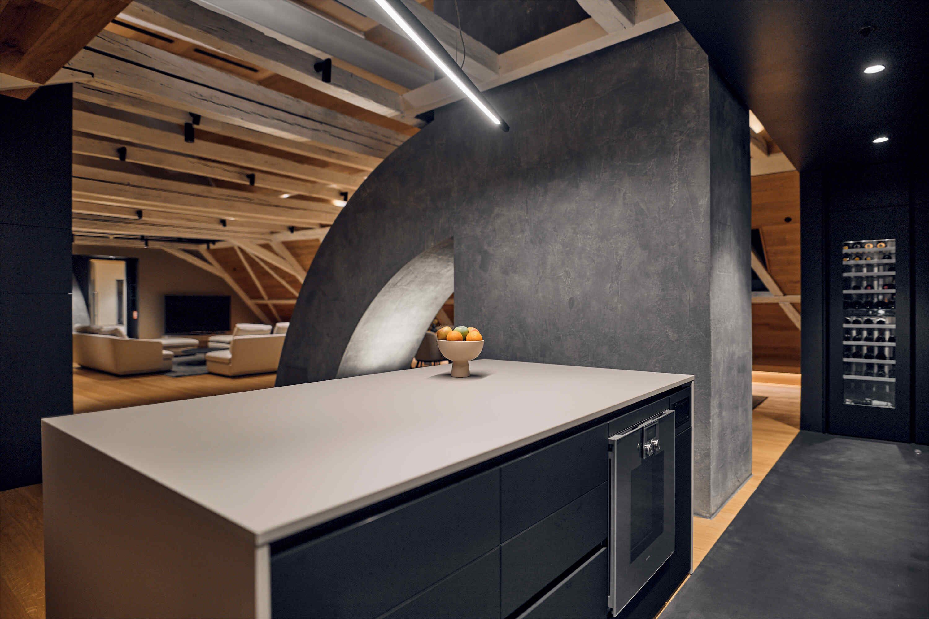 A modern kitchen with a large island, dark cabinetry, and a curved wall structure.