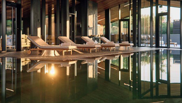 Una piscina interior moderna con sillones de descanso y grandes ventanales.