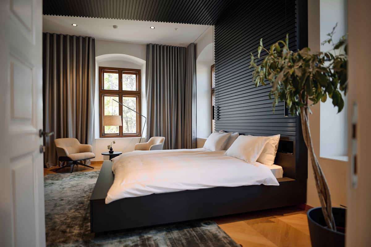 Ein modernes Schlafzimmer mit einem großen Bett, zwei Stühlen, einem kleinen Tisch und einem Blumentopf.
