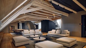 Un salón tipo ático con vigas de madera a la vista, zona de comedor y un amplio ventanal que proporciona luz natural.