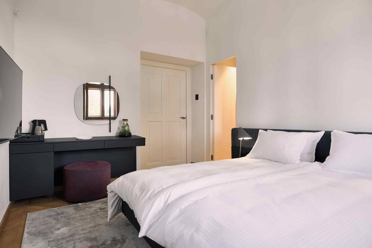 Ein Schlafzimmer mit Bett, Schreibtisch, Stuhl, Spiegel und Tür.