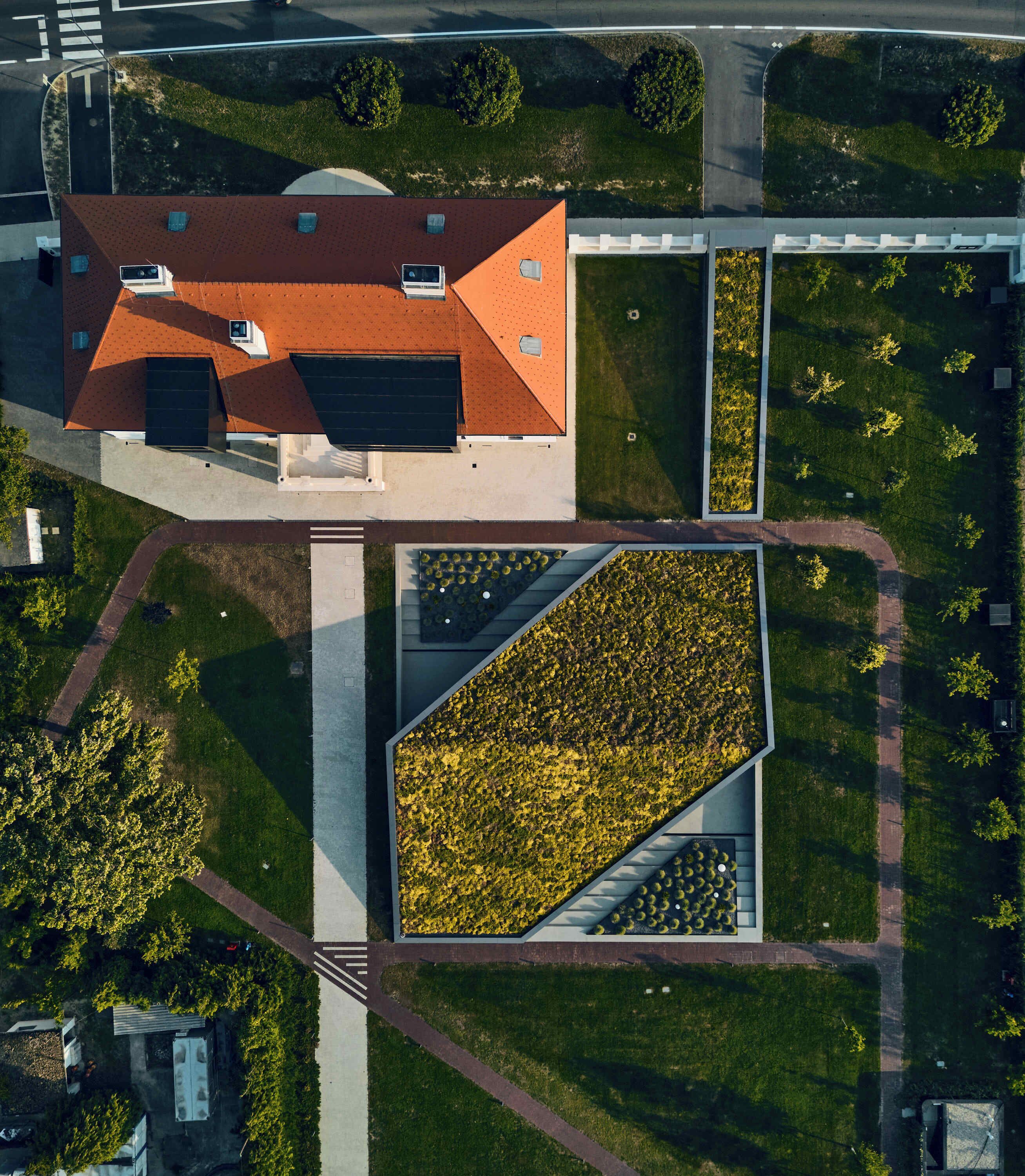 An aerial view of a building with a red roof, surrounded by green lawns and a rectangular garden area.