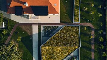 An aerial view of a building with a red roof, surrounded by green lawns and a rectangular garden area.
