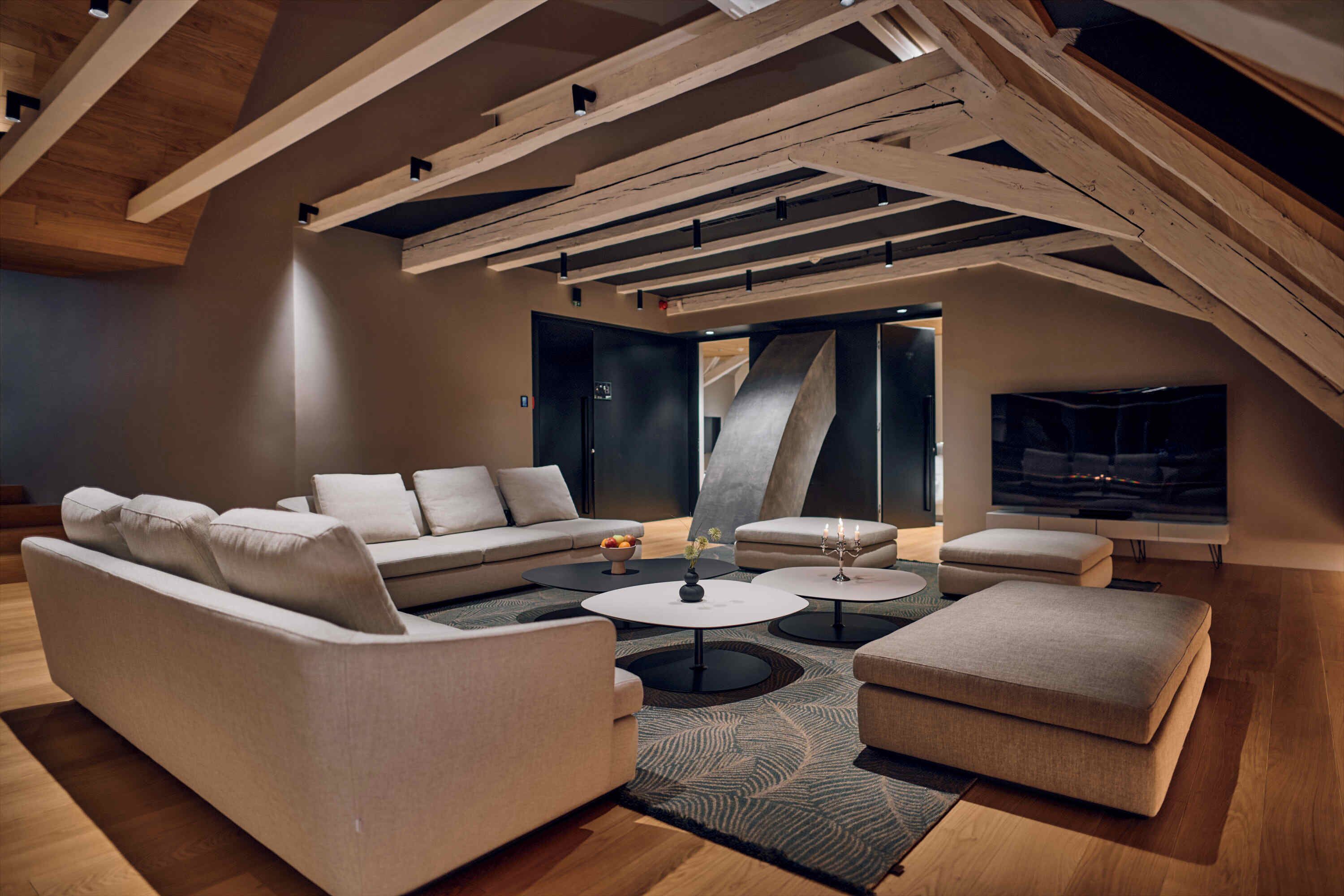 Una sala de estar moderna con techo alto, vigas a la vista, un sofá modular, una mesa de centro y un televisor de pantalla plana.