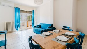 Un comedor con una mesa de madera preparada para cuatro personas, un sofá azul y vistas a un balcón a través de un ventanal.