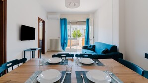 Un comedor con una mesa de madera dispuesta para cuatro personas, un sofá azul y un televisor montado en la pared.