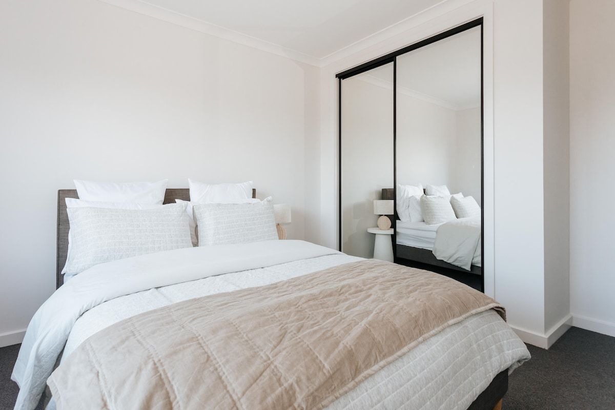 A bedroom with a bed, a large mirror, and a nightstand with a lamp.