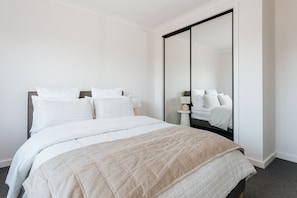 A bedroom with a bed, a large mirror, and a nightstand with a lamp.