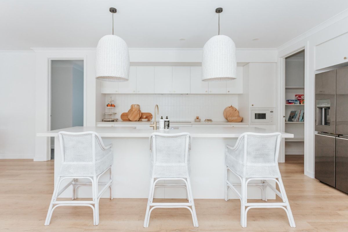 A modern kitchen with white cabinetry, a central island with bar stools, pendant lighting, and a stainless steel refrigerator.