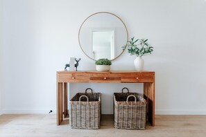 A wooden console table with a round mirror, two wicker baskets, a potted plant, and a small decorative item.