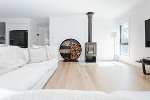 A modern living room with a white sofa, a round wood-burning stove, and a large window.