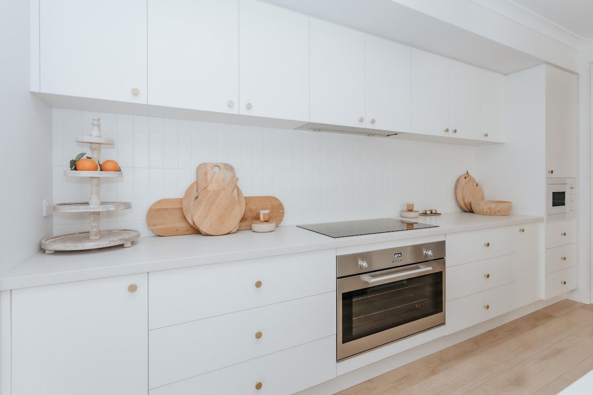 Una cocina moderna con armarios blancos, horno empotrado y tabla de cortar de madera.