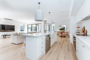 A modern kitchen with white cabinetry, a central island, stainless steel appliances, pendant lighting, and a dining area with wooden furniture.