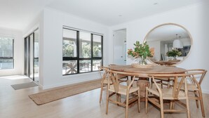 Un comedor moderno con una mesa redonda de madera y sillas, un espejo grande y vistas a través de un ventanal.