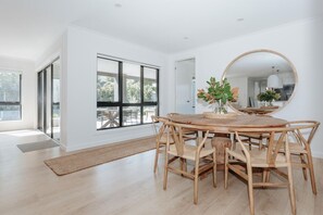 A modern dining area with a round wooden table and chairs, a large mirror, and a view through a glass door.