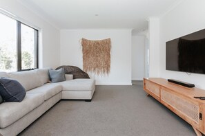 Un salon moderne avec un canapé d’angle, un téléviseur à écran plat et une décoration murale tissée.