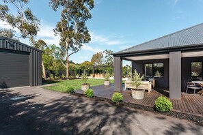 A modern outdoor patio area with a covered seating area, a wooden deck, and a landscaped garden.