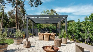Un espacio patio al aire libre con una pérgola, mobiliario de mimbre y un hogar para fuego.