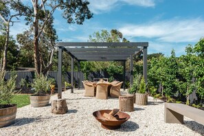 An outdoor patio area with a pergola, wicker furniture, and a fire pit.