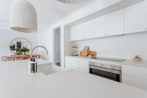 A modern kitchen with white cabinetry, a built-in oven, and a hanging light fixture.