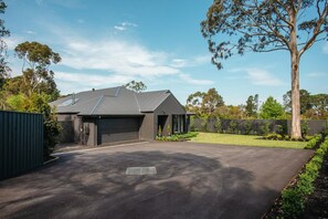 A modern house with a garage, driveway, and a fenced yard with trees.