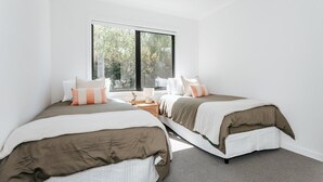 Un dormitorio con dos camas, un ventanal y vista a árboles.