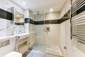 Ein modernes Badezimmer mit einer Duschkabine aus Glas, einem мраморном Waschplatz und einem eingebauten Spiegel.