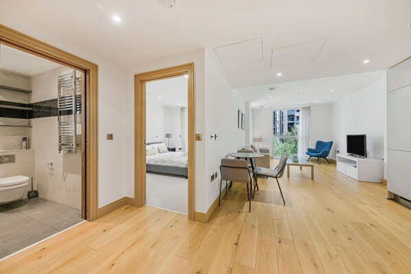 A modern apartment with a wooden floor, a bathroom with a towel rack, a dining area with a table and chairs, a living room with a TV, and a bedroom with a bed and window. - Paddington Ex LUX Flats  (London)