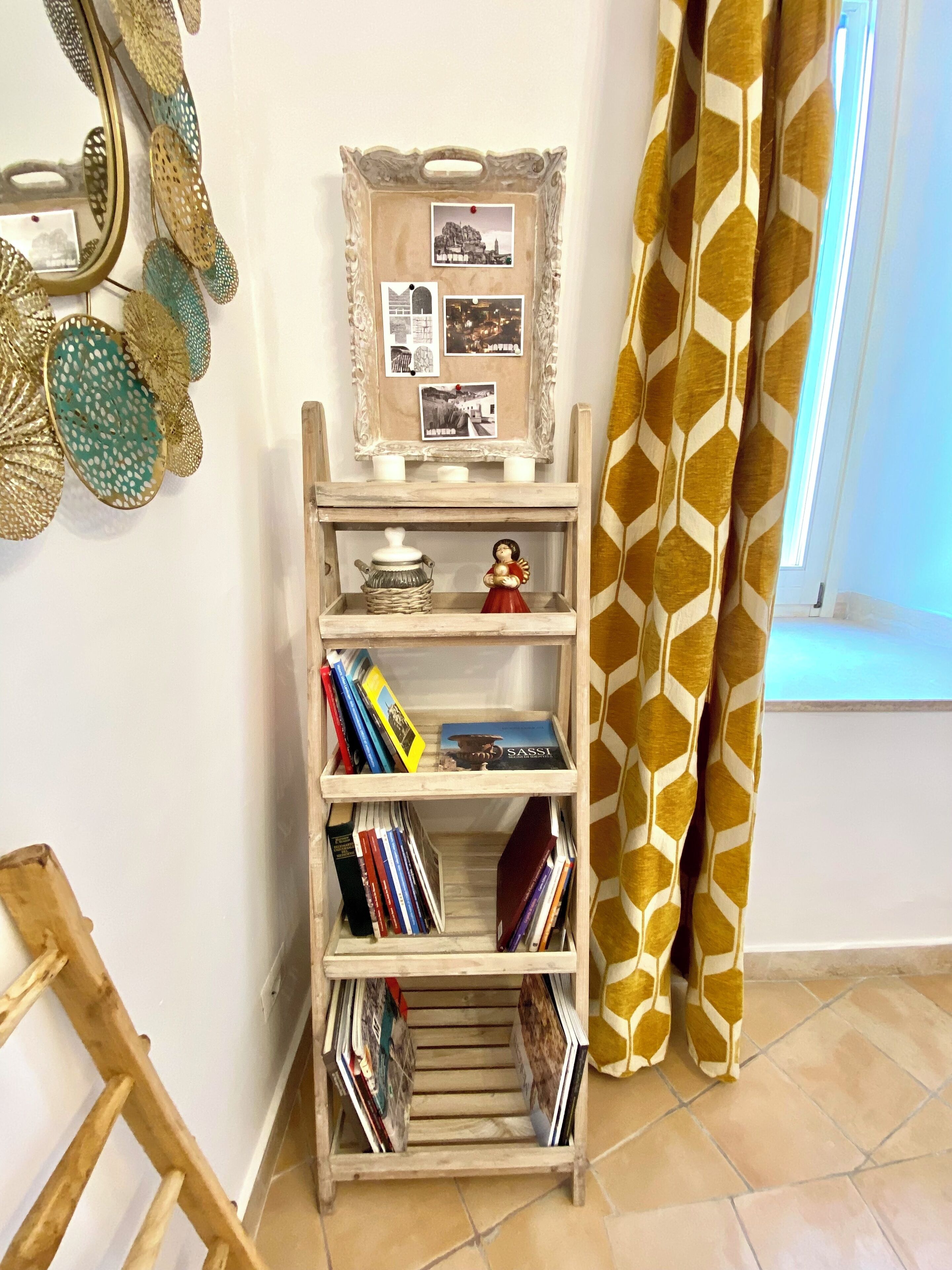 Een houten boekenkast met boeken en decoratieve objecten, een fotocollage in een lijst aan de muur, en een gordijn met patroon.
