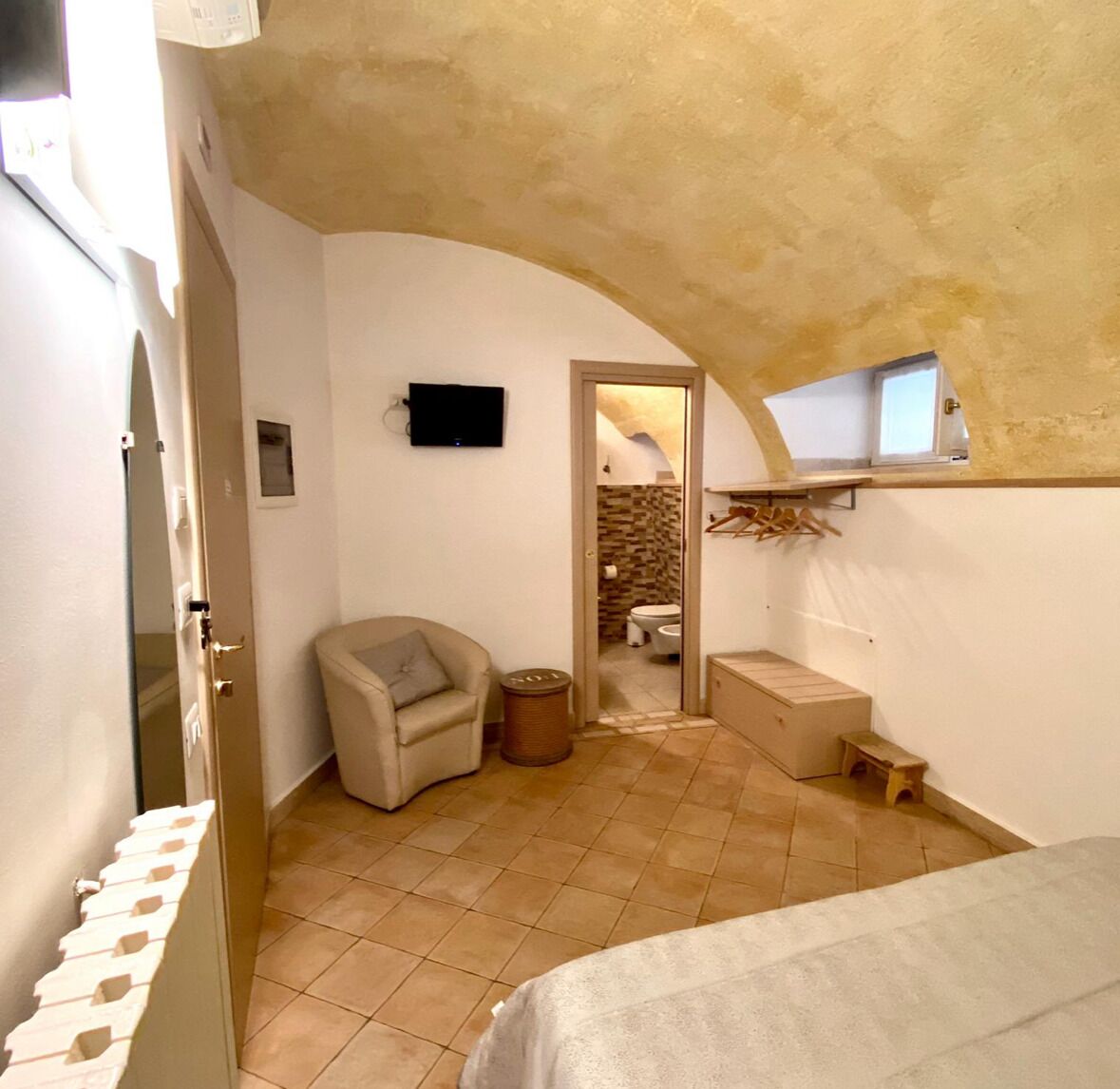 A compact bedroom with a bed, a chair, a small table, and a television.