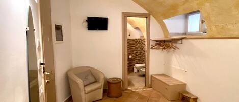 A compact bedroom with a bed, a chair, a small table, and a television.