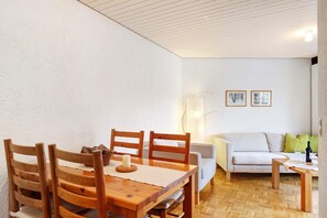Un comedor con mesa y sillas de madera, un sofá y una mesita con una botella y un vaso.