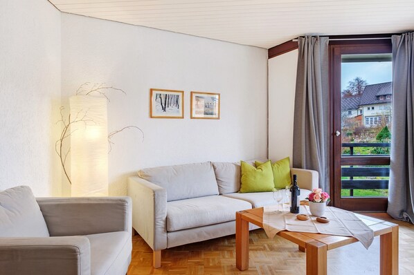Un salon avec un canapé, une table basse et une vue sur une maison, visible à travers une porte vitrée.