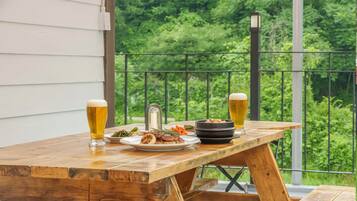 A wooden table with food and drinks on a balcony with a metal railing and greenery in the background.