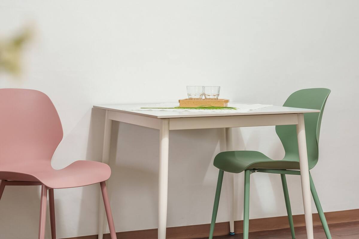 Une table blanche avec deux chaises, une rose et une verte, et une petite plante posée sur la table.
