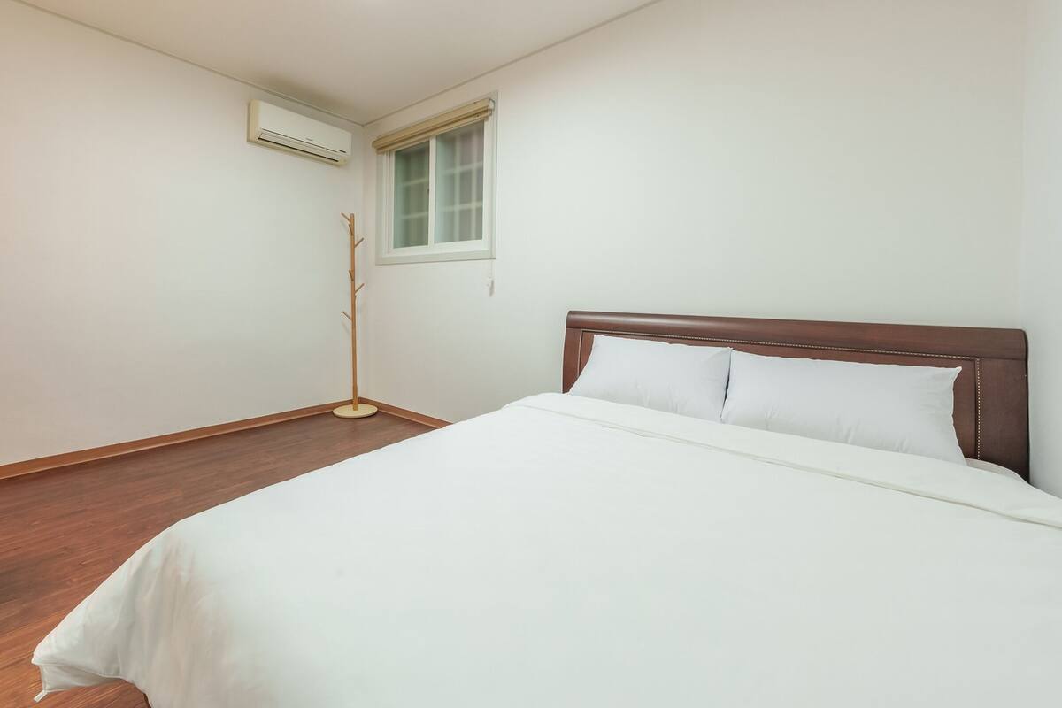 Une chambre d’hôtel comprenant un lit, une table de chevet avec une lampe, un lampadaire et un appareil de climatisation.
