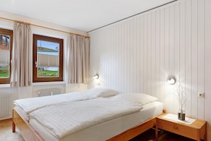 A bedroom with a bed, a bedside table, a nightstand, a window with curtains, and a wall-mounted light fixture. - Ferienwohnung 2 mit Balkon – barrierefrei, 2 Schlafzimmer, Küche, Bernau im Schwarzwald (Bernau im Schwarzwald)